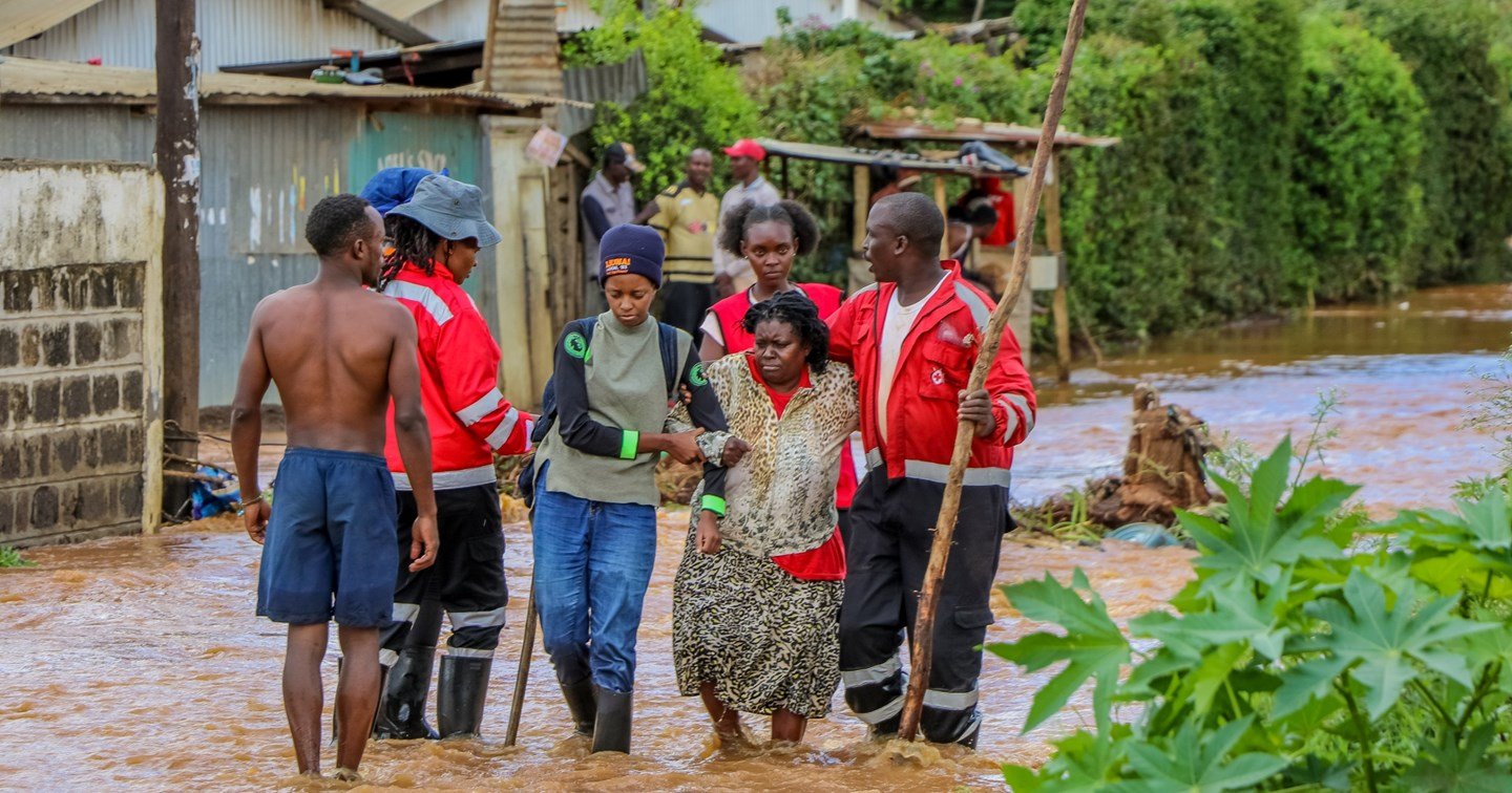 Red Cross volunteers help a person walk through flooding.