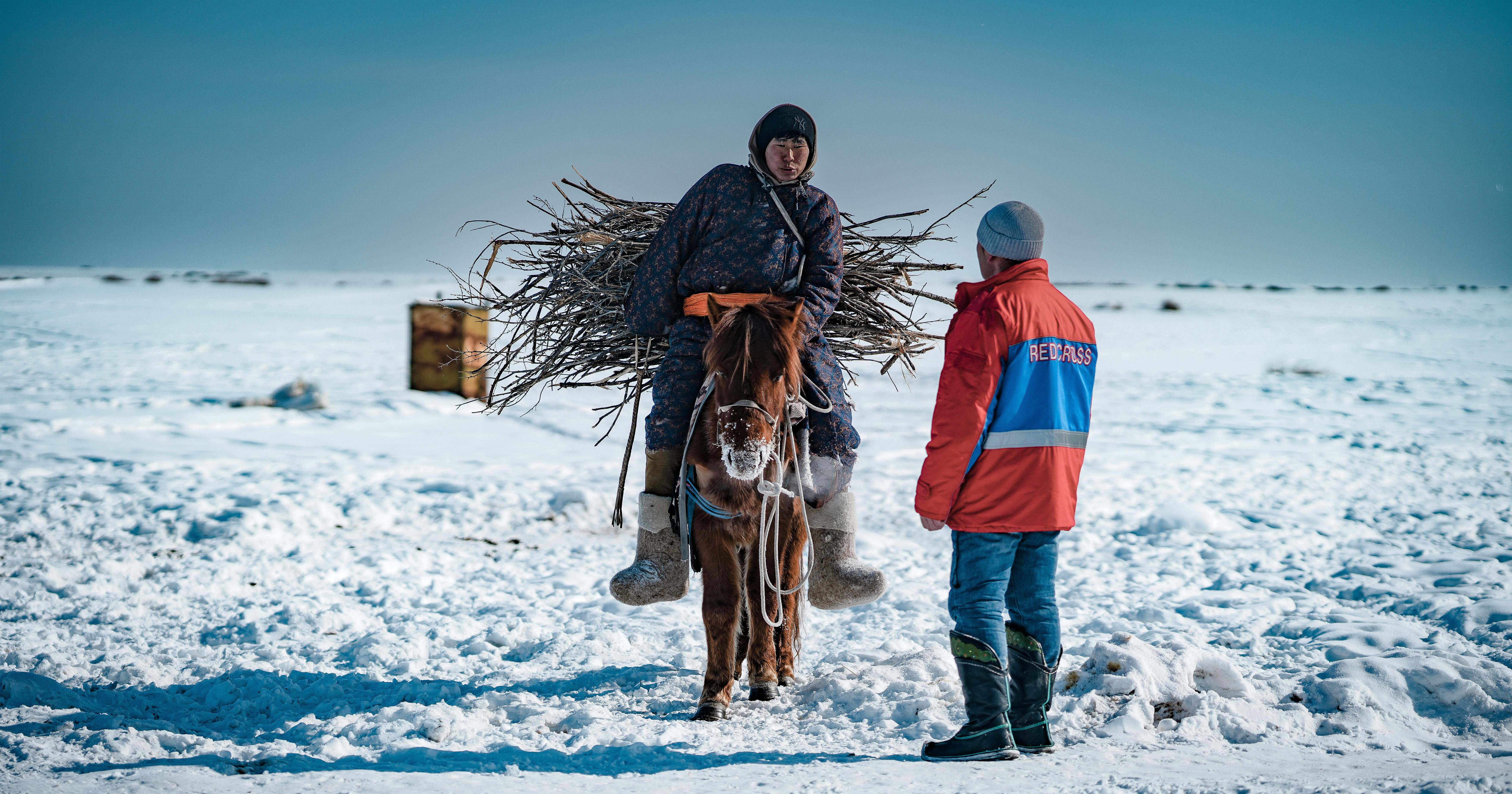 A Red Cross volunteer talking to a Mongolian person in a wintry landscape.