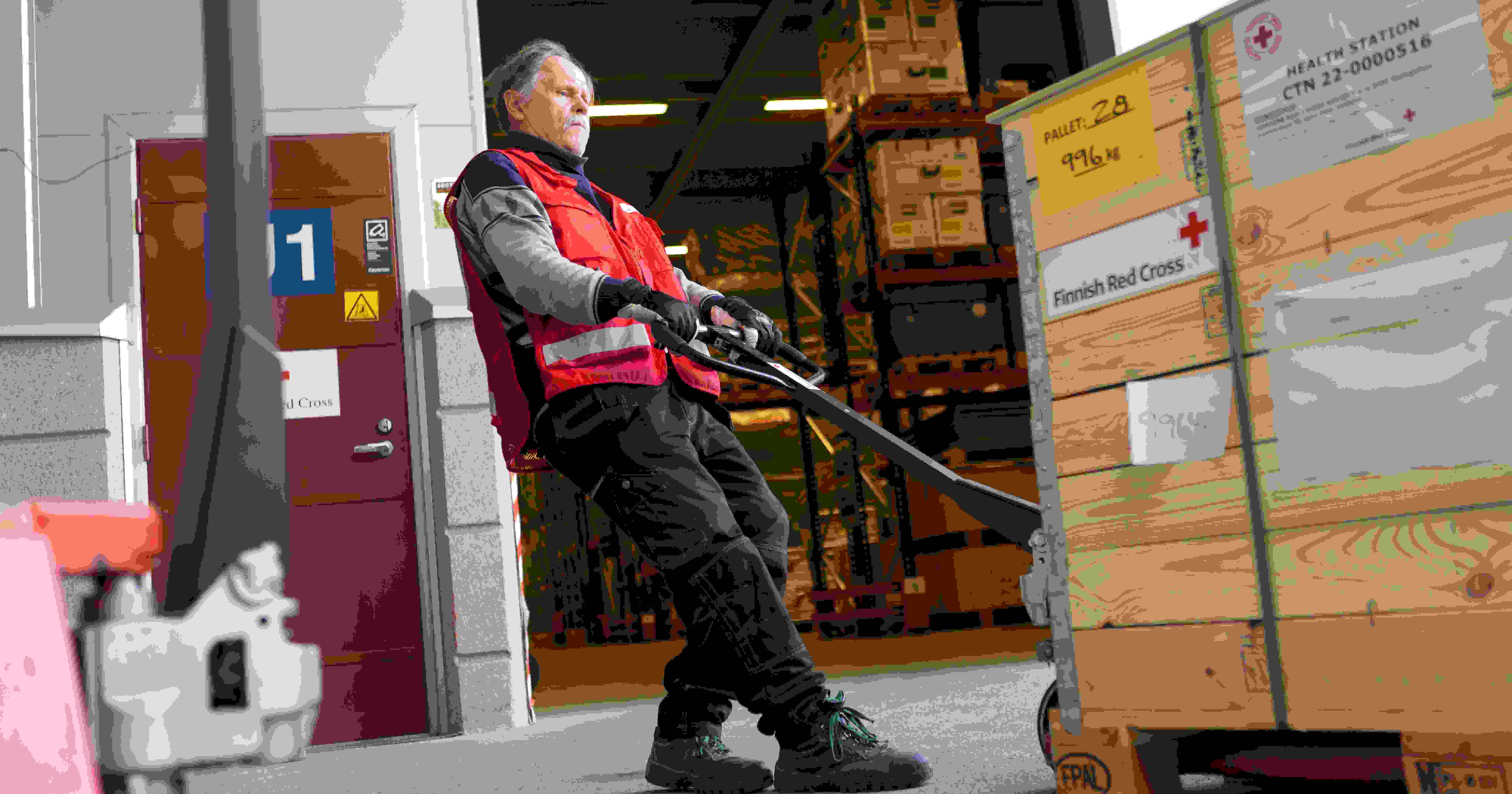 Red Cross employee moving a load with a pallet jack. The boxes read "Health station".