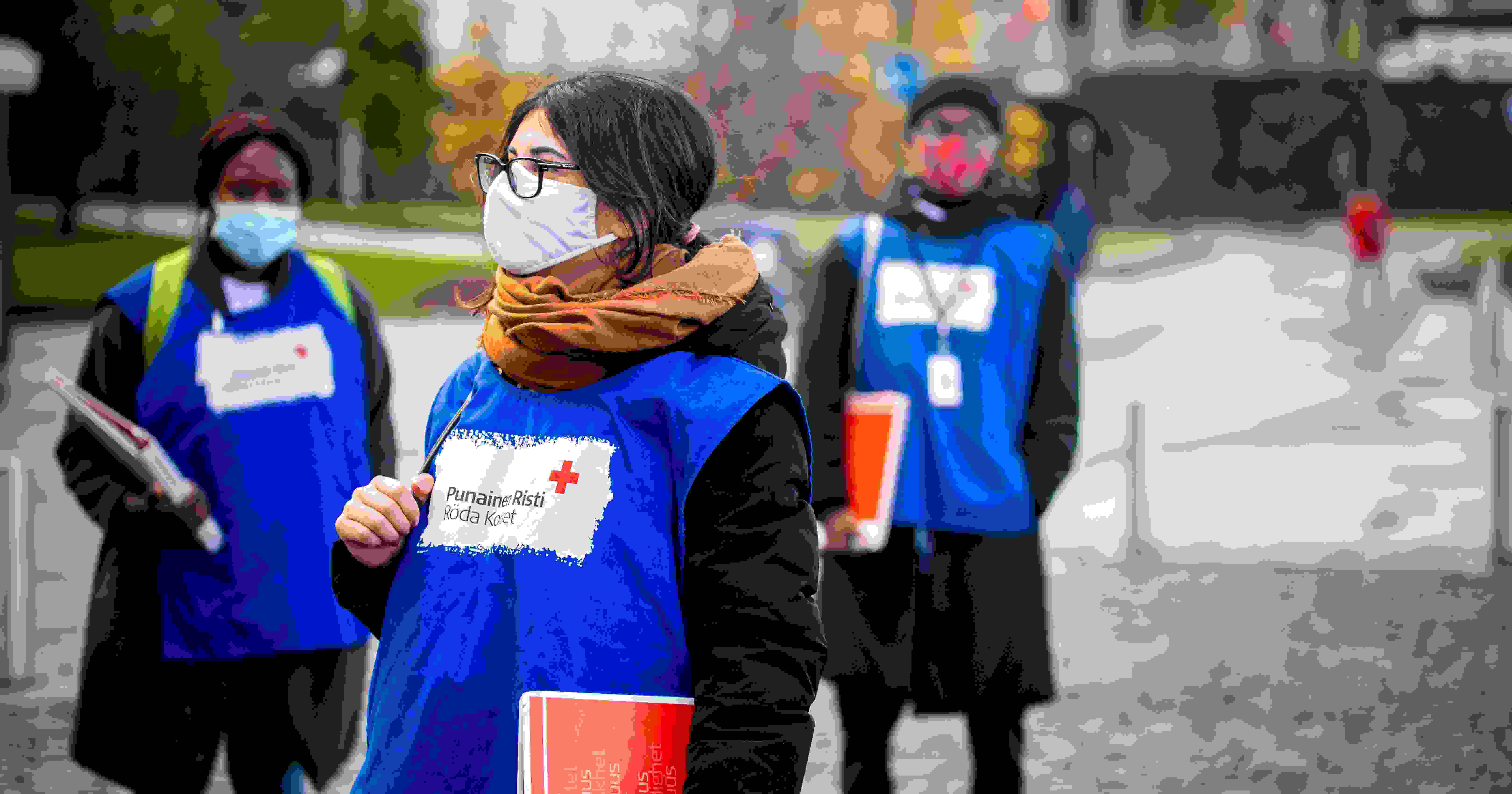 Three Red Cross face-to-face fundraisers standing on a street with red folders and wearing blue Red Cross face-to-face fundraiser vests.