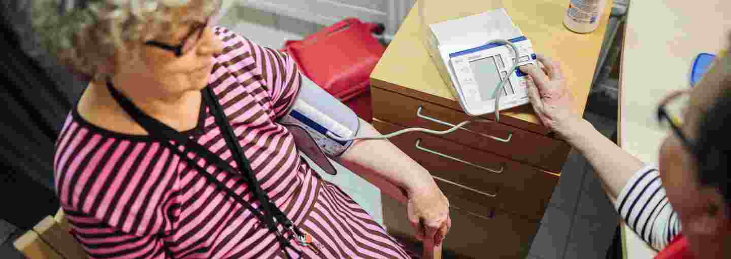 A woman wearing a Red Cross volunteer vest taking the blood pressure of an elderly woman.