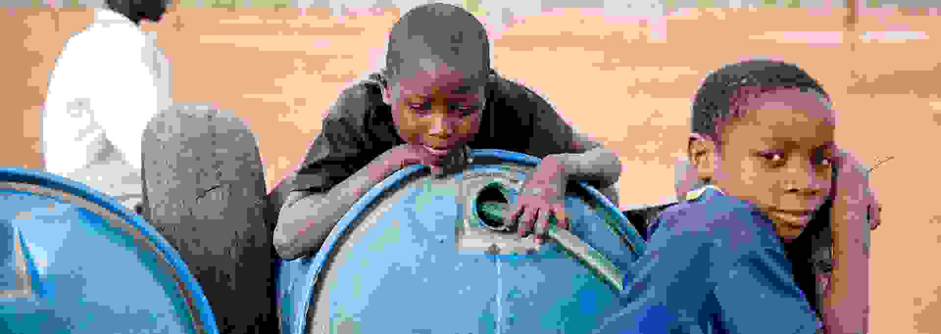 Three Zimbabwean boys by clean water barrels.