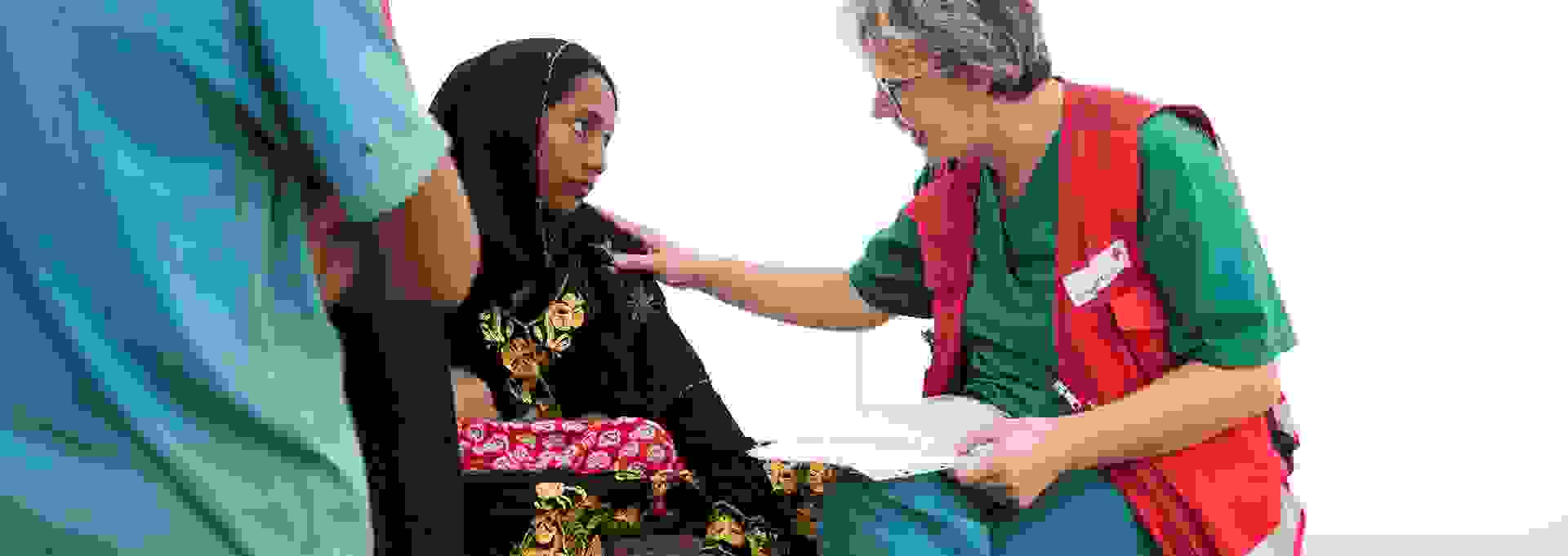 A young Bangladeshi woman is talking to a Red Cross aid worker at a field hospital.
