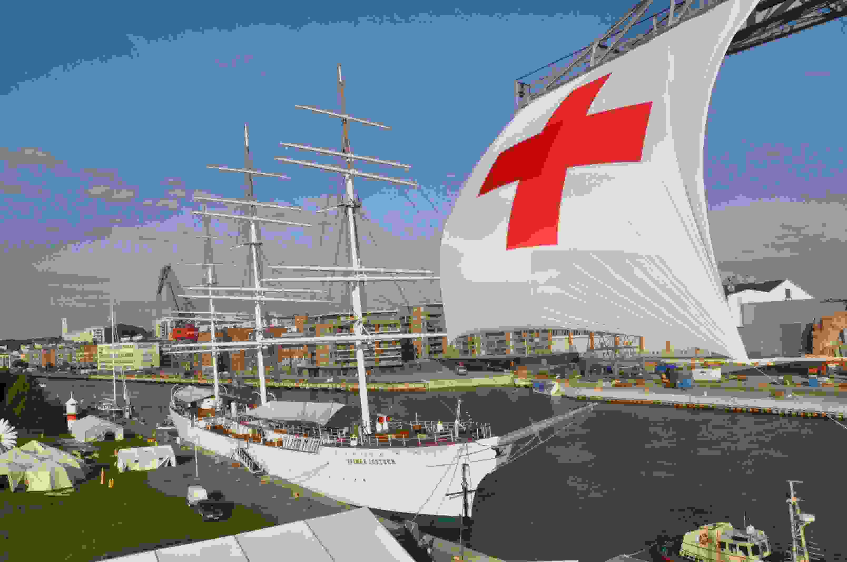 Suomen Joutsen laiva Aurajoessa, jonka edessä jättimäinen lippu, jossa punainen risti.