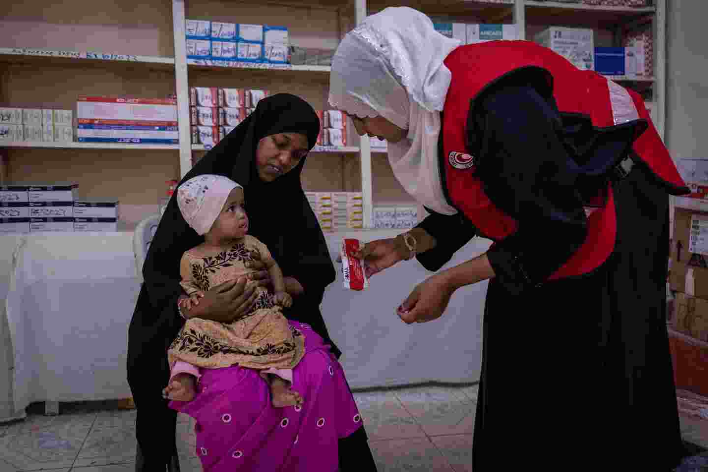 A child and a mother at a Red Crescent clinic. A nurse giving food to a child.