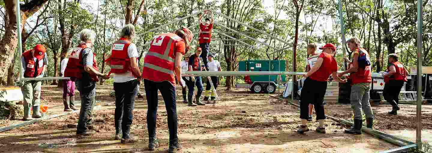 Thirteen Red Cross aid workers building a hospital tent in a sunny clearing in Bangladesh.