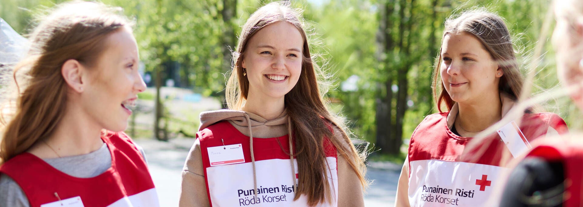 Red Cross volunteer collection box fundraisers are smiling outdoors in sunny weather.