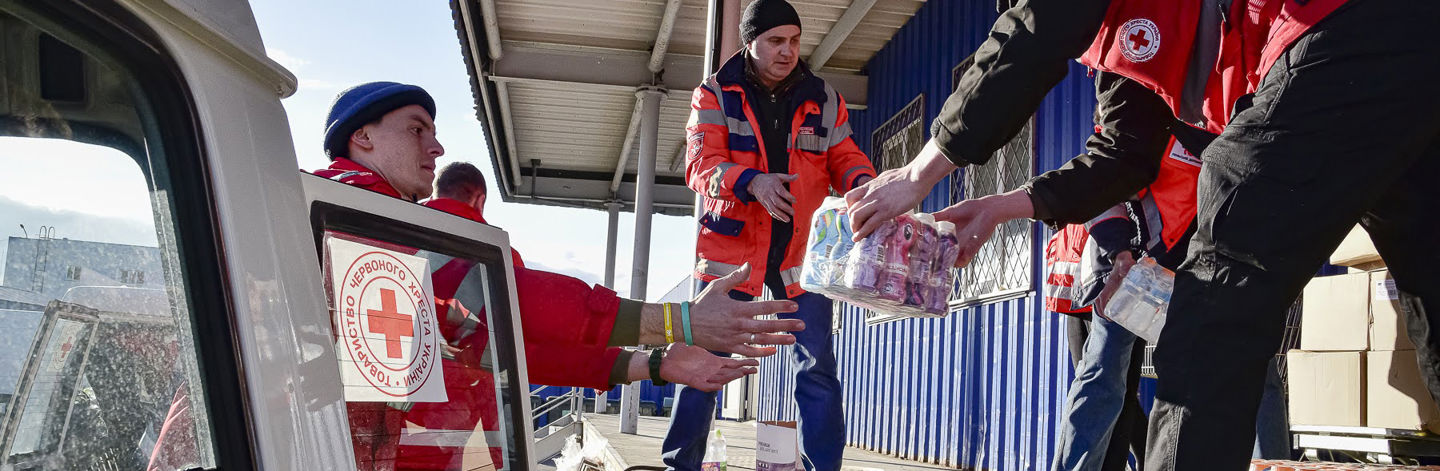 A woman dressed in Red Crescent clothing is handing soap to women wearing headscarves in Afghanistan.