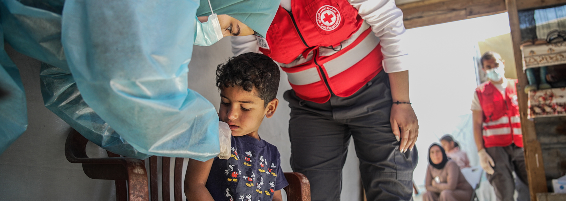 Two Red Cross volunteers in red vests, holding collection boxes. They are next to an about two-metre tall collection box.