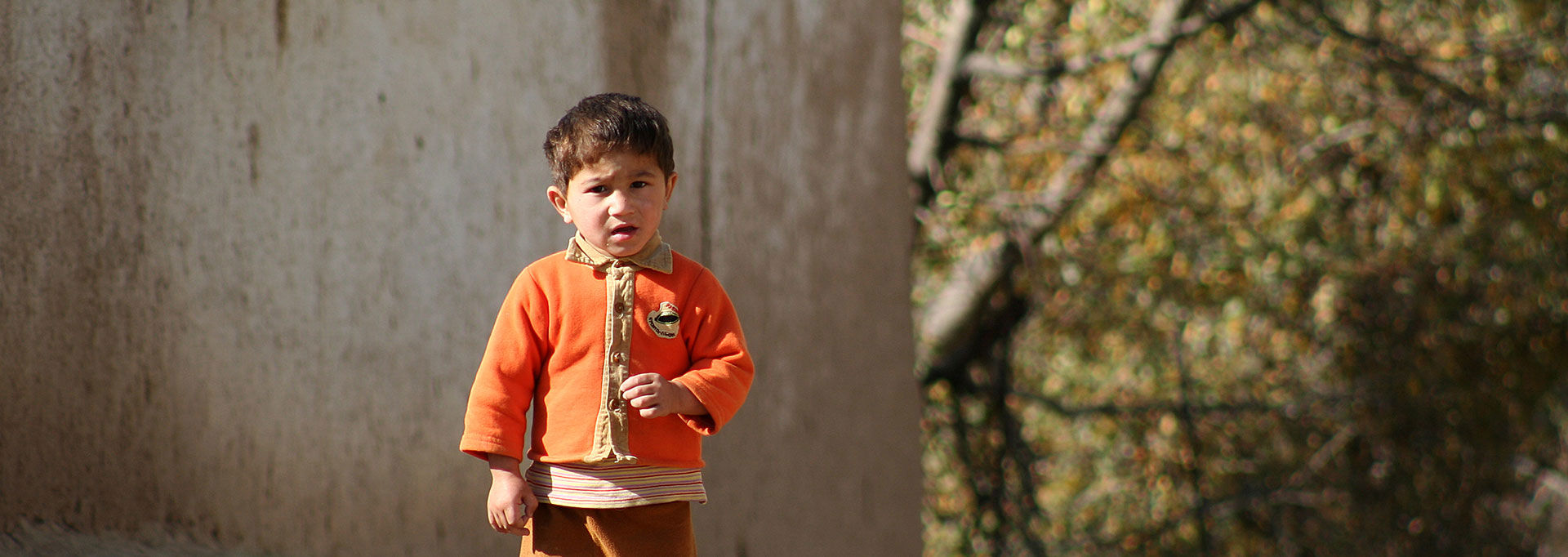 A child standing in front of a house and looking at the camera.
