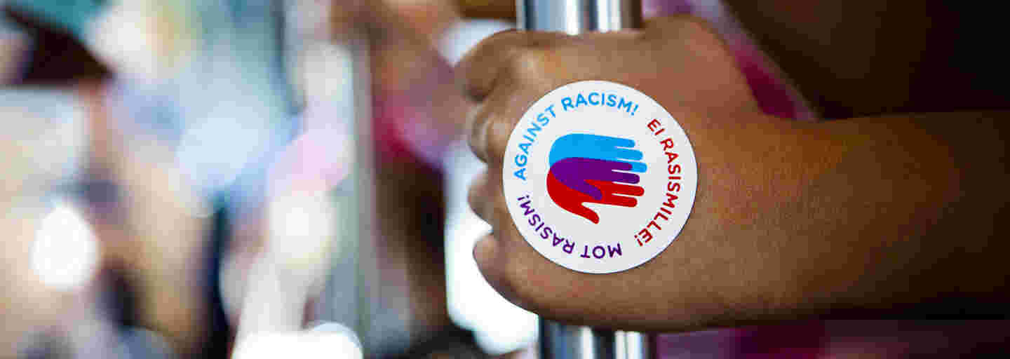 Hand with an Against Racism! logo sticker holding a bar in a tram.