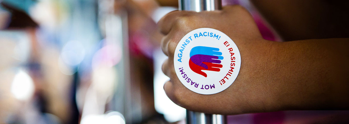 Hand with an Against Racism! logo sticker holding a bar in a tram.