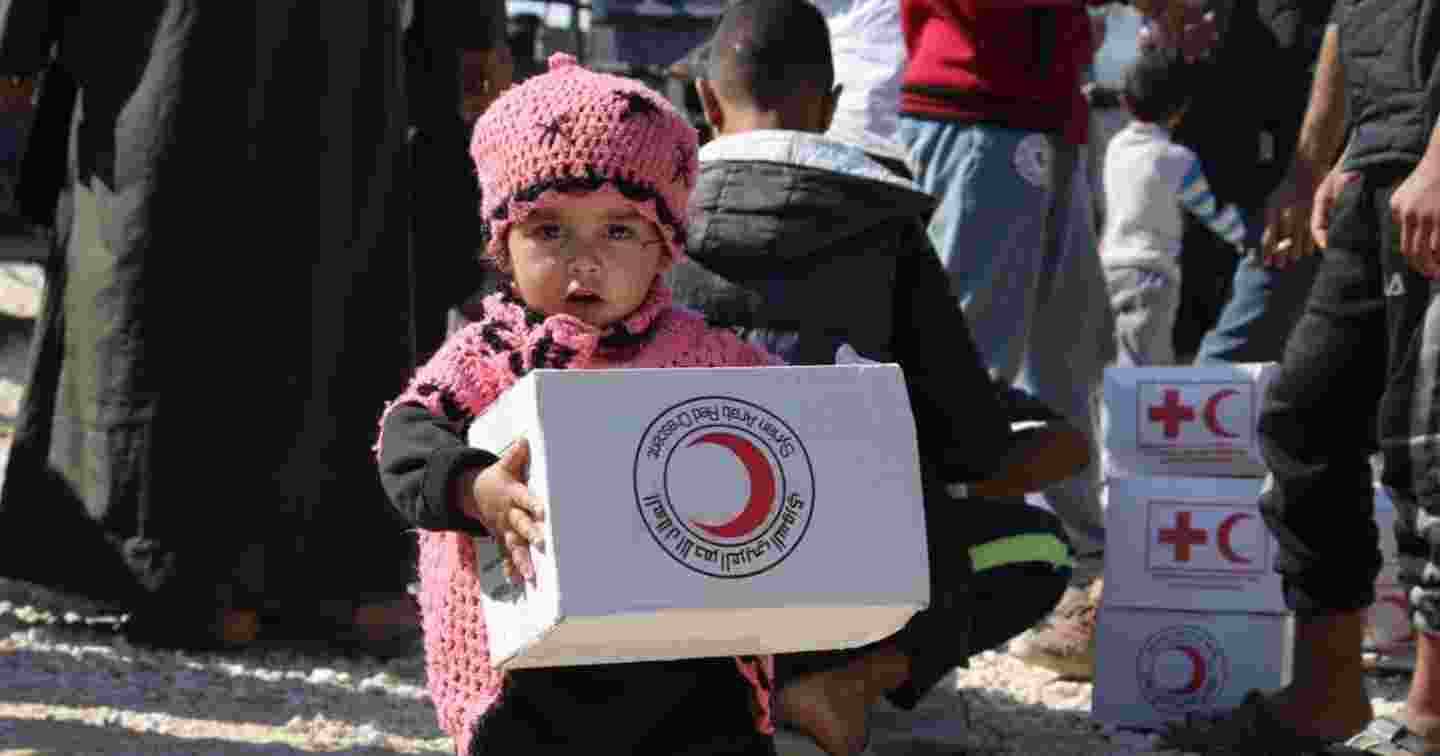 A small Syrian child holding a Red Cross aid package