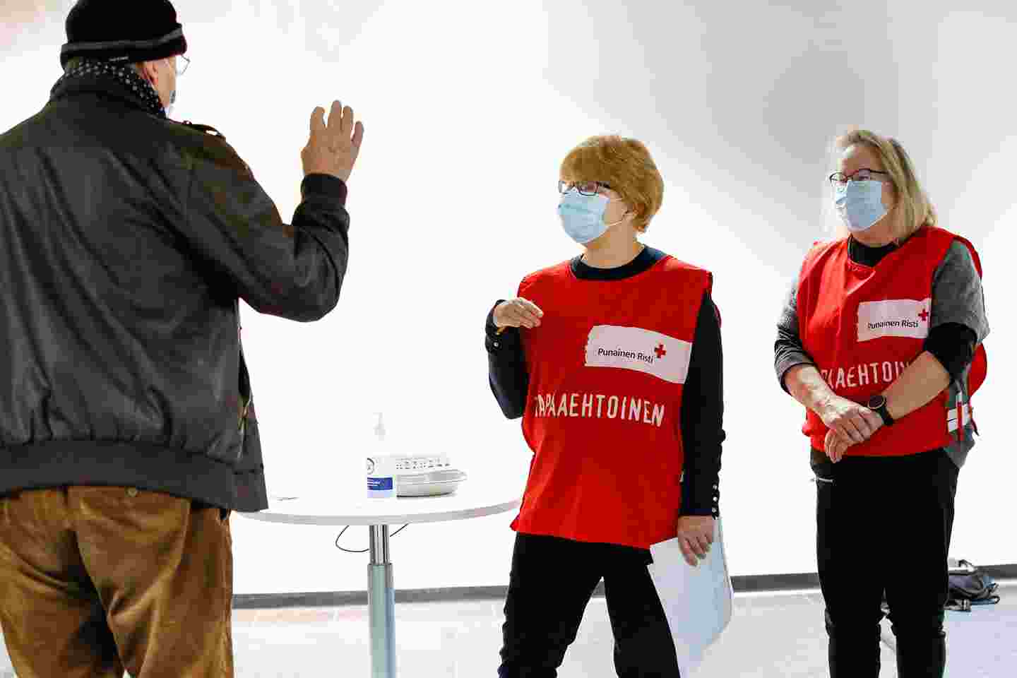 Person coming to be vaccinated talking with two Red Cross volunteers.