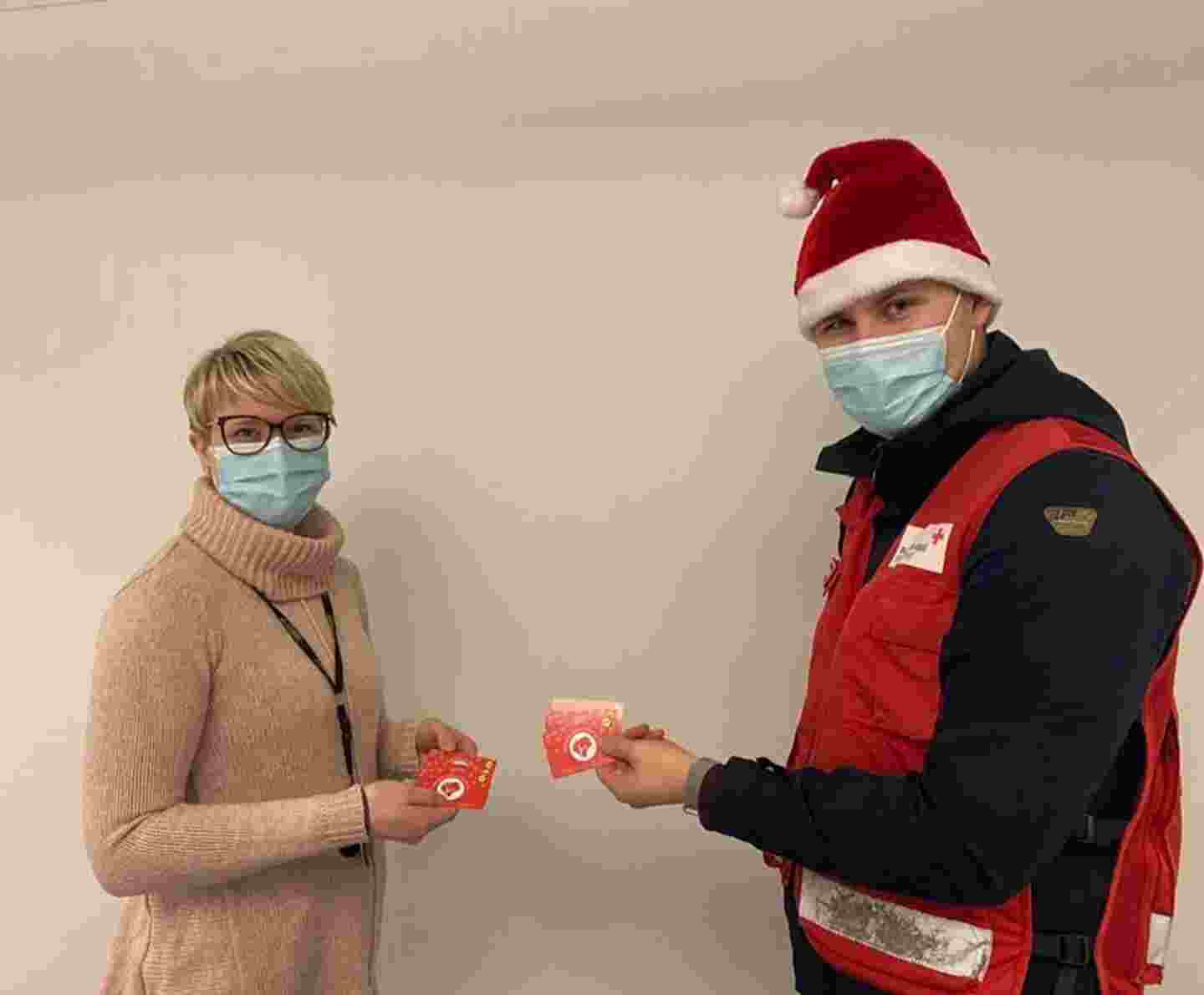 Two people wearing masks and holding food vouchers. One person is wearing a Red Cross vest and Christmas hat.