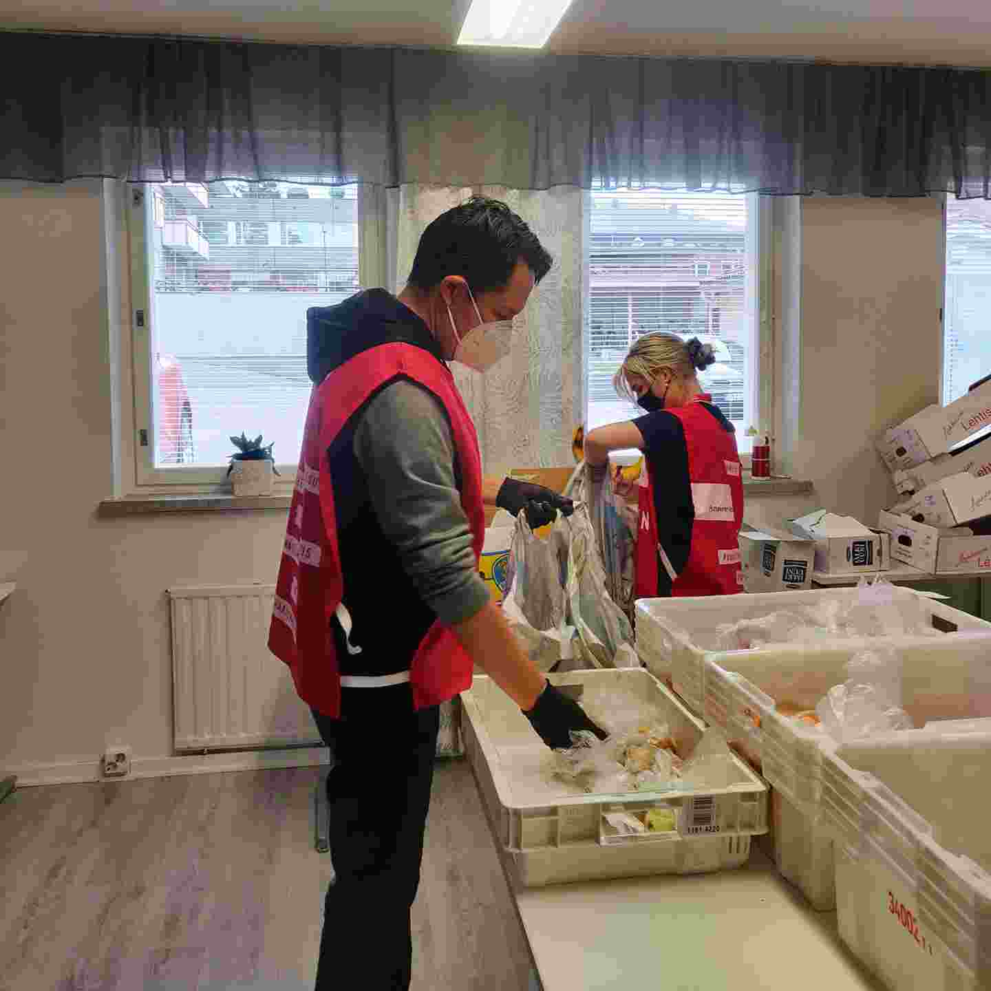 Person wearing a Red Cross volunteer vest packing food items at a table.