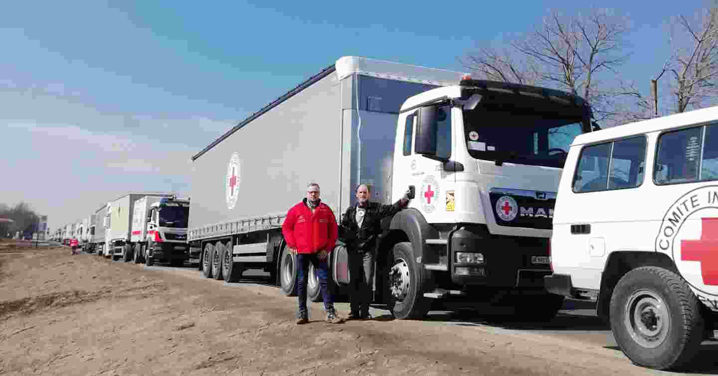 Two Red Cross employees standing in front of a Red Cross truck convoy.