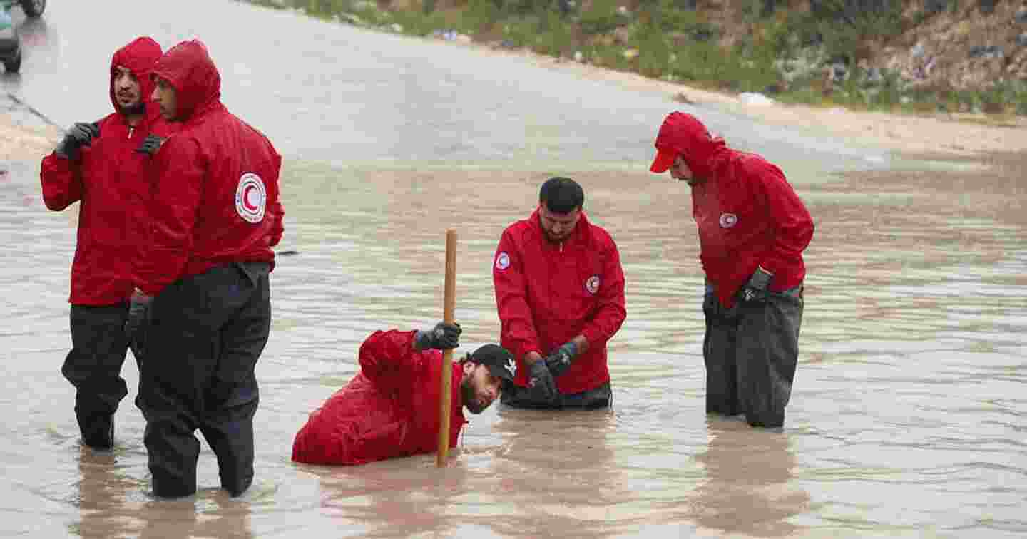 People in Red Crescent vests standing in the middle of flood water.