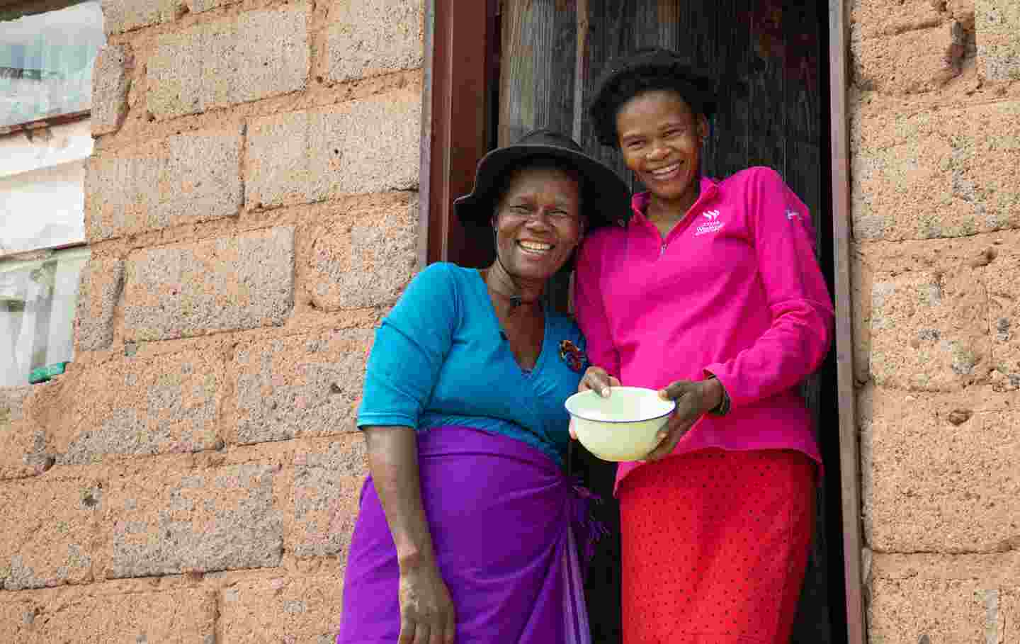 Two people smiling in front of their home in Eswatini.