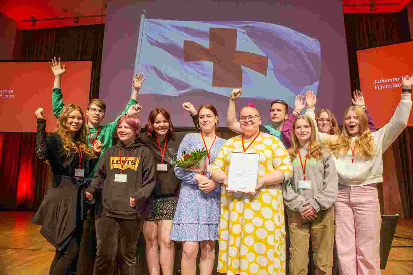 Young, smiling Red Cross volunteers accepting an award on a stage.