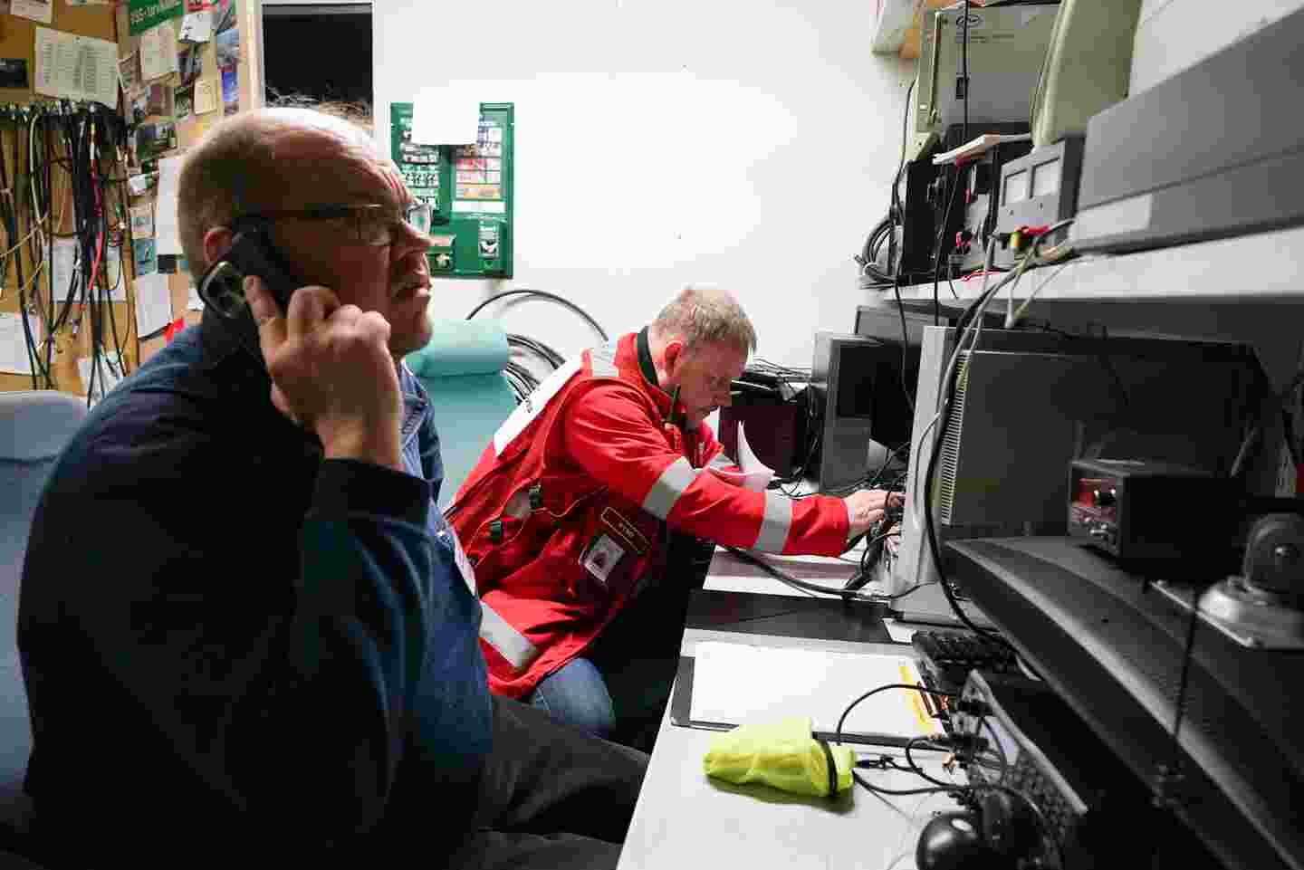 Volunteers of the Red Cross and the Voluntary Rescue Service in a technical room, surrounded by different devices. One of the volunteers is speaking on the phone.