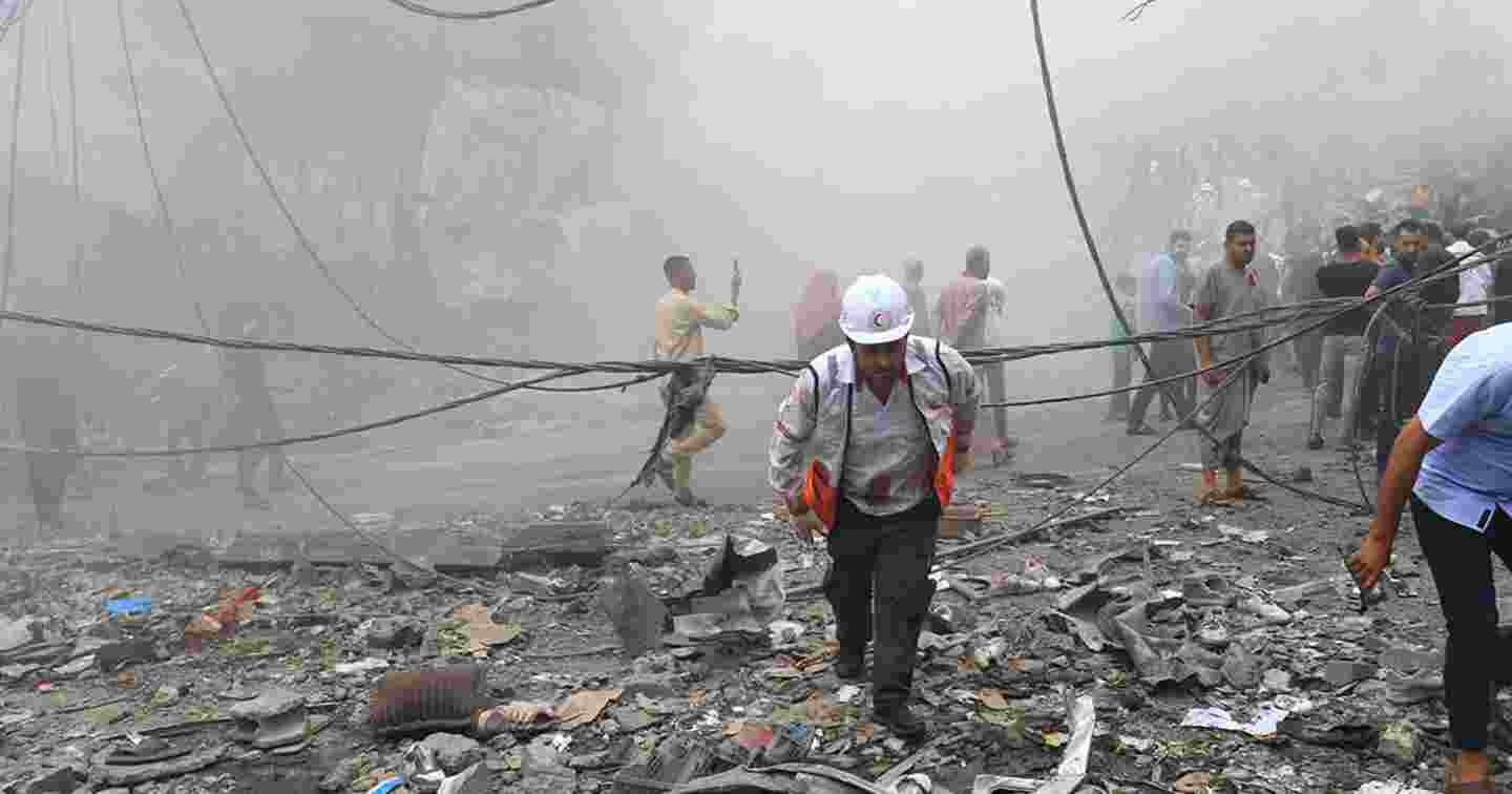 A volunteer, wearing Red Crescent's helmet and vest, walking in the middle of ruins and dust.