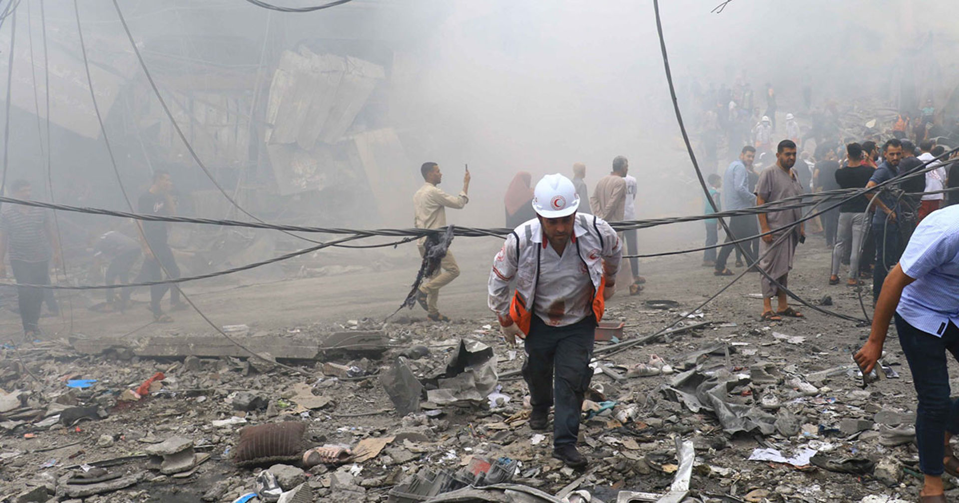 A volunteer, wearing Red Crescent's helmet and vest, walking in the middle of ruins and dust.