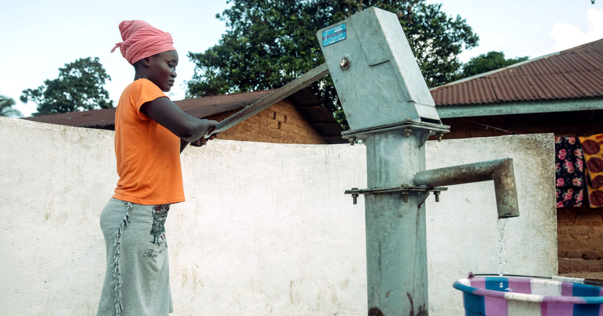 A woman is pumping water from a steel pump into a multicoloured water container.