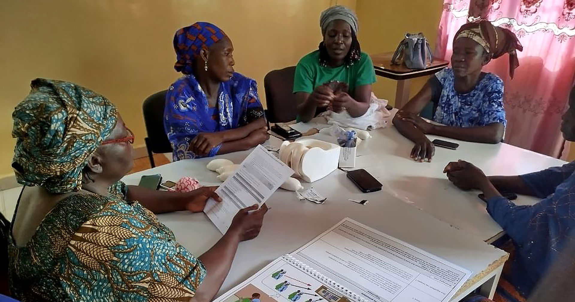 A group of women are sitting at a table reading reproductive health guides.