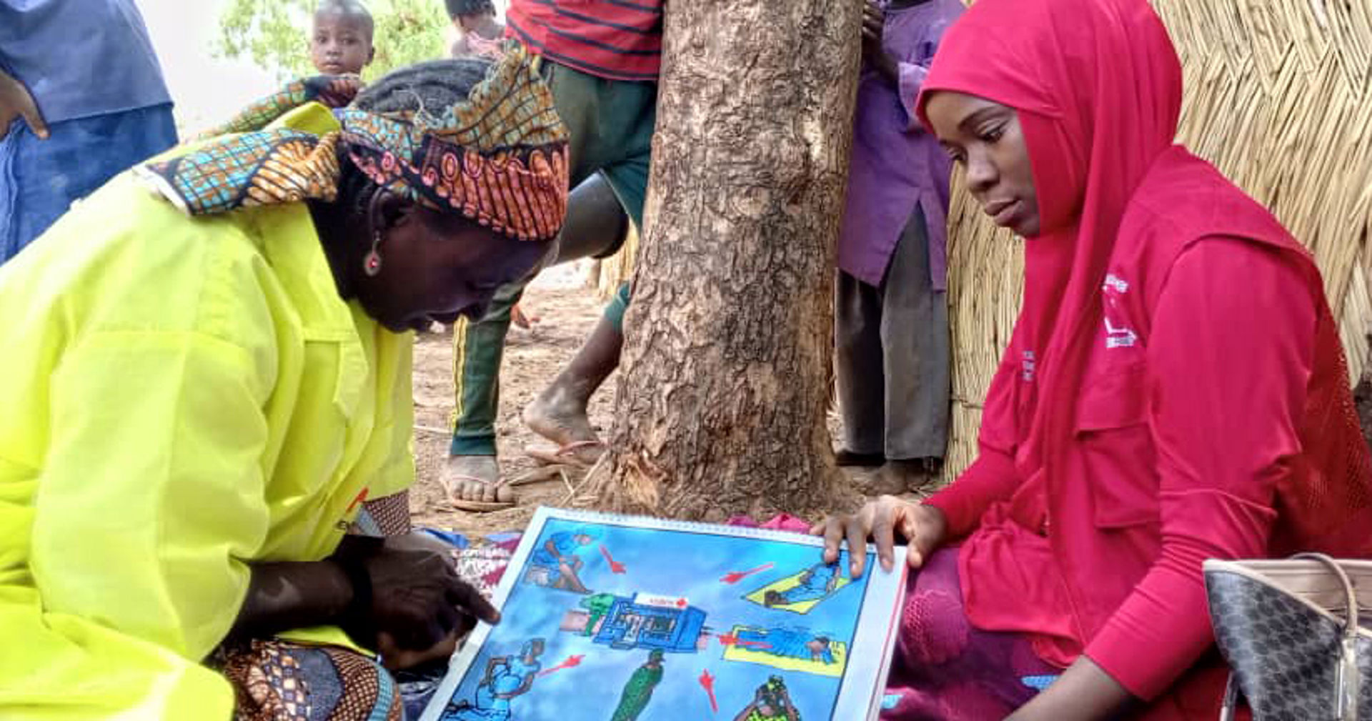 A traditional birth assistant trained by the Red Cross, wearing red clothes, is showing a picture of safe childbirth to a woman.