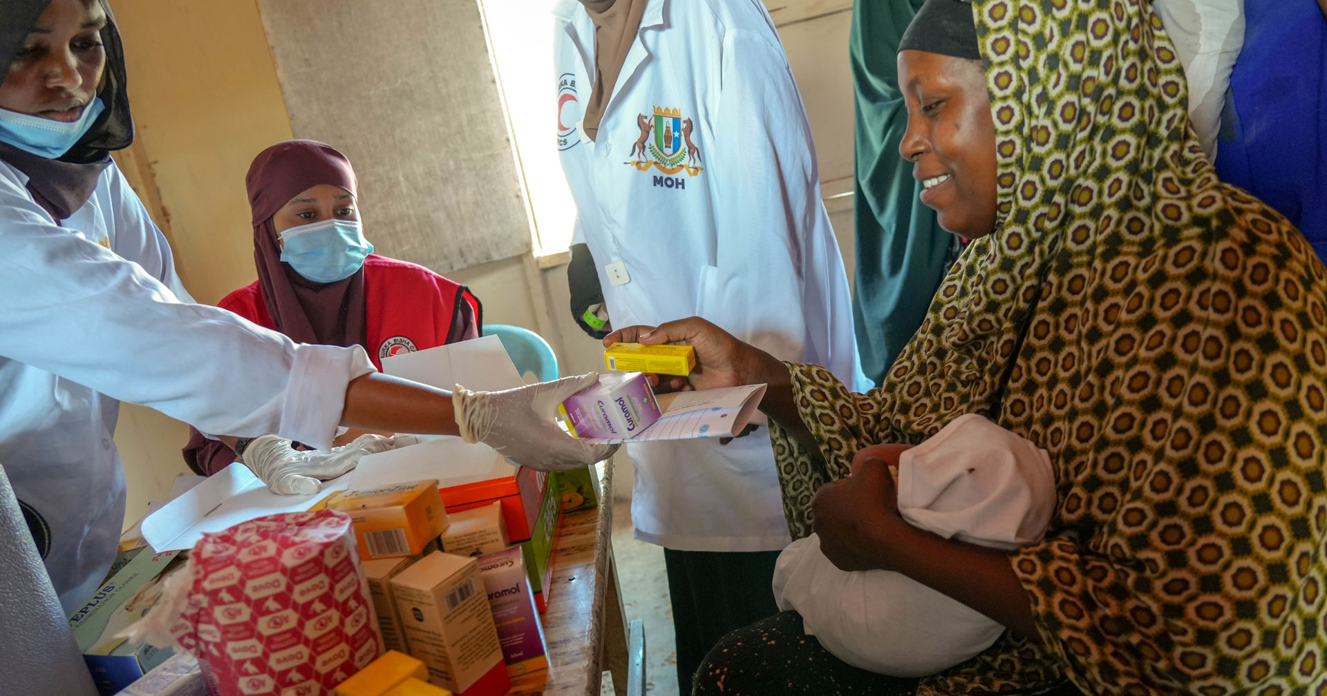 A mother is receiving medicine for her newborn, surrounded by health care staff.
