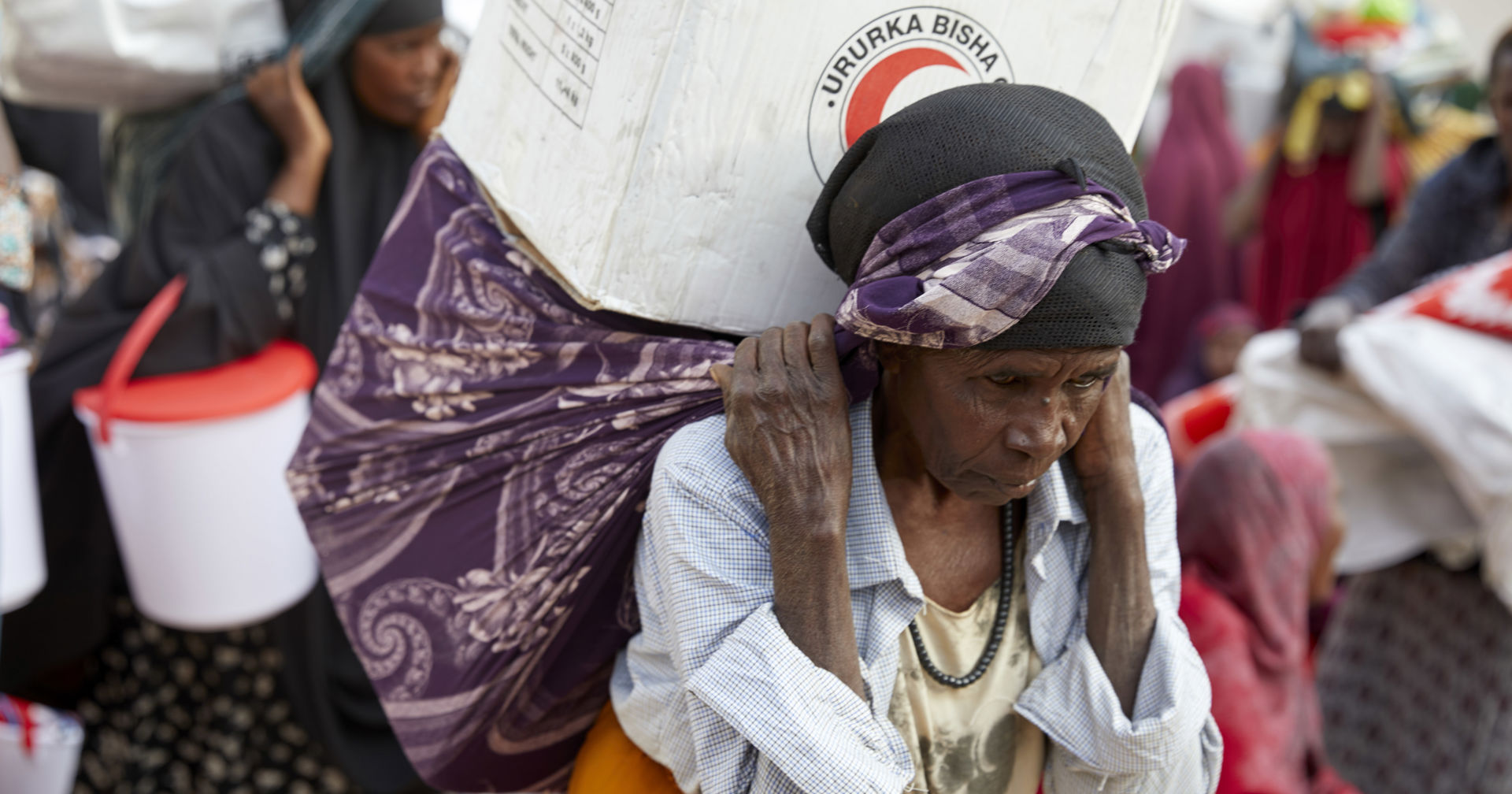 A woman is carrying a big cardboard box with a scarf.