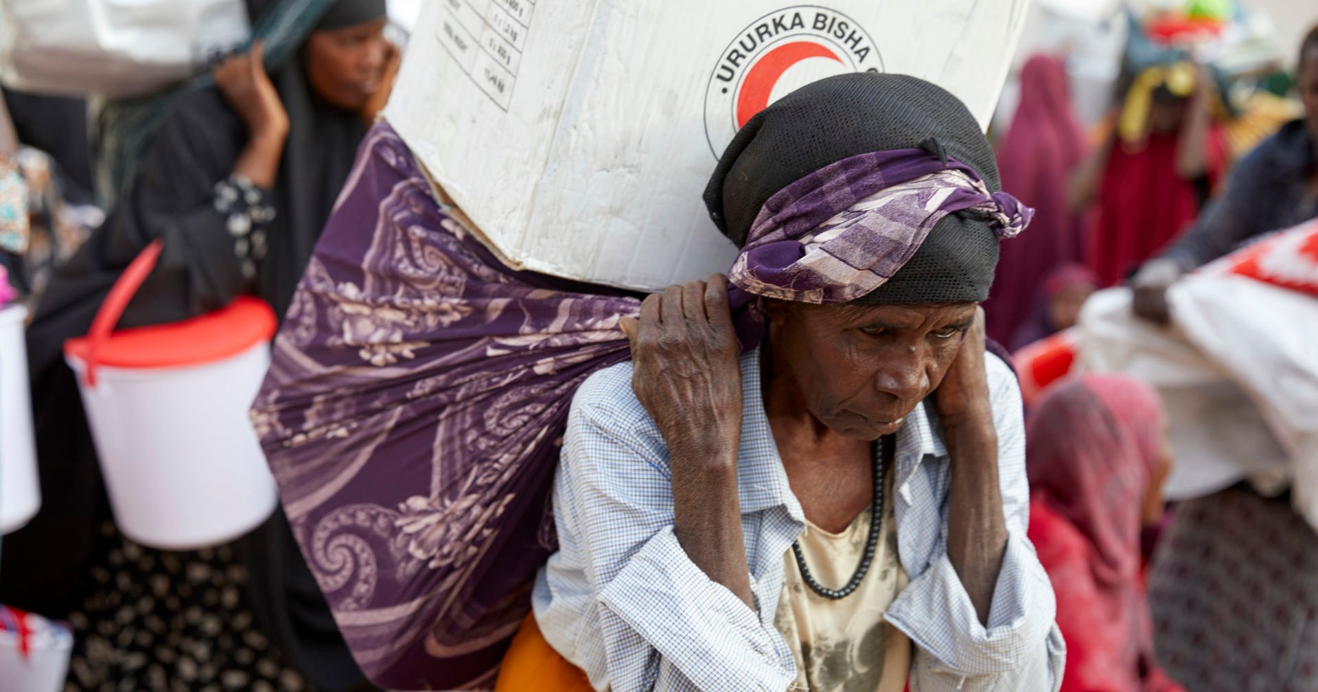 A woman is carrying a big cardboard box with a scarf.