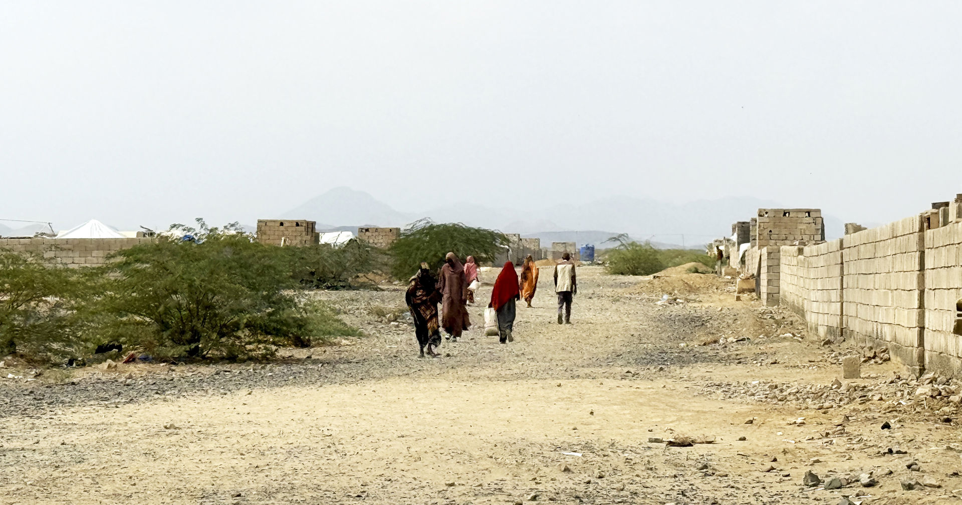 A group of people walk toward the camera on a dry, rocky road in Sudan.