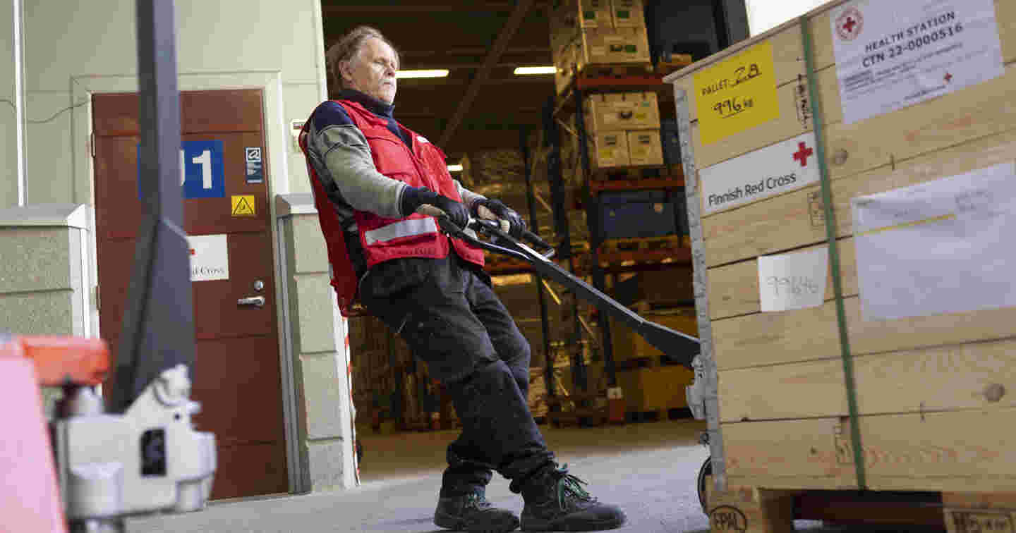 Red Cross employee moving a load with a pallet jack. The boxes read "Health station".