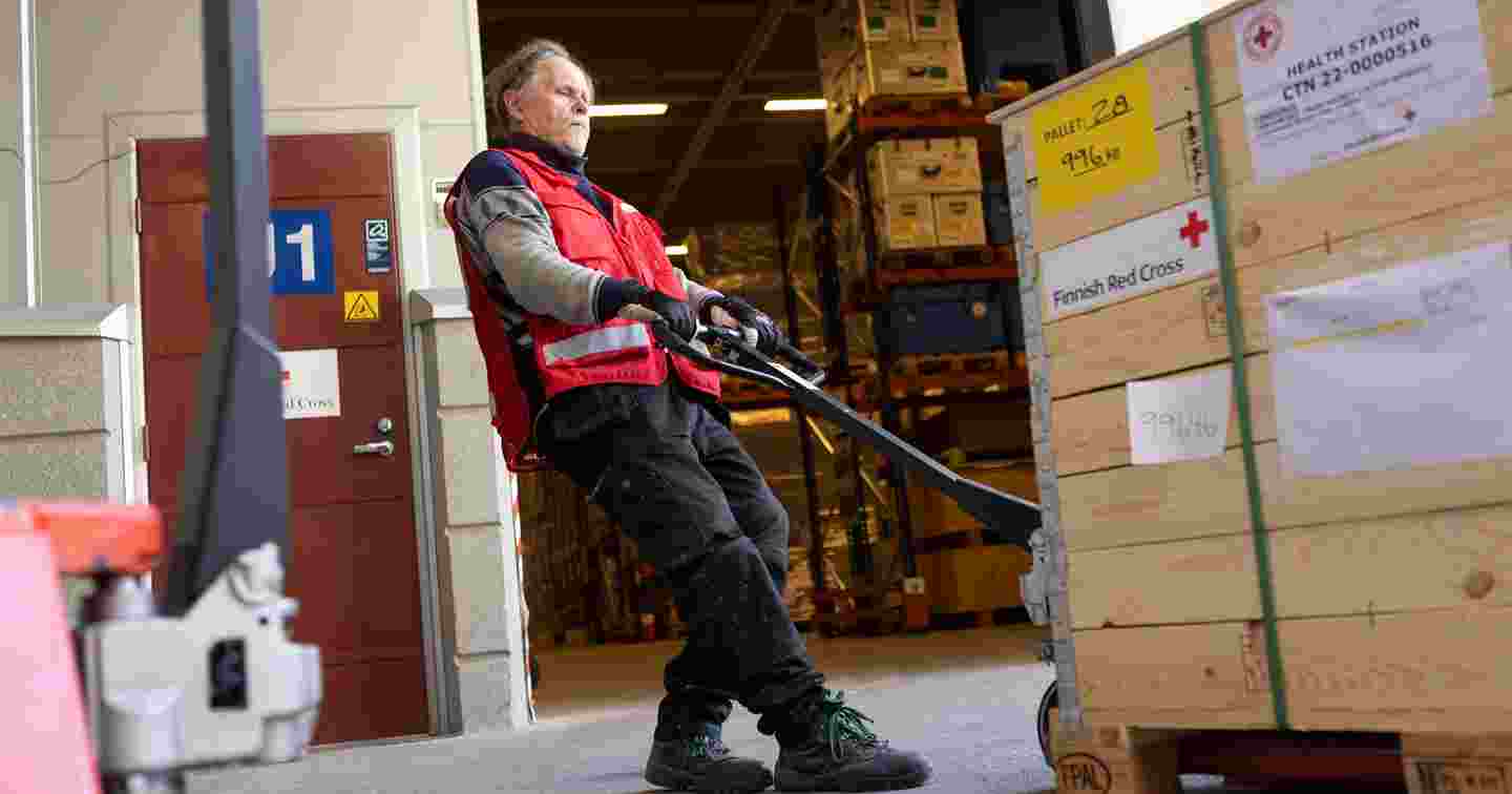 Red Cross employee moving a load with a pallet jack. The boxes read "Health station".
