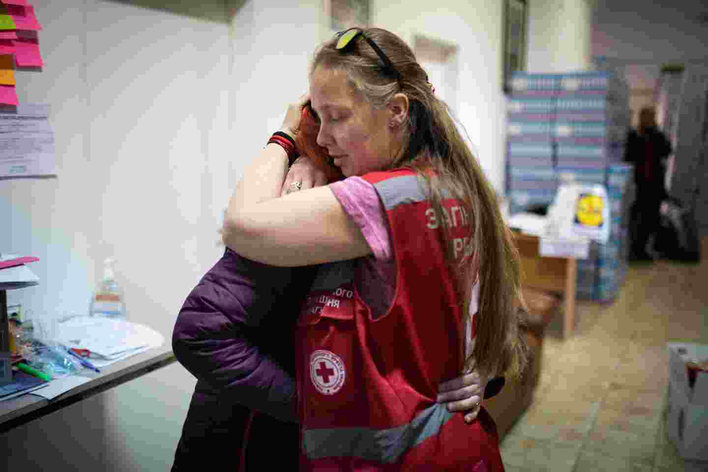 A person wearing Red Cross clothing hugging another person.