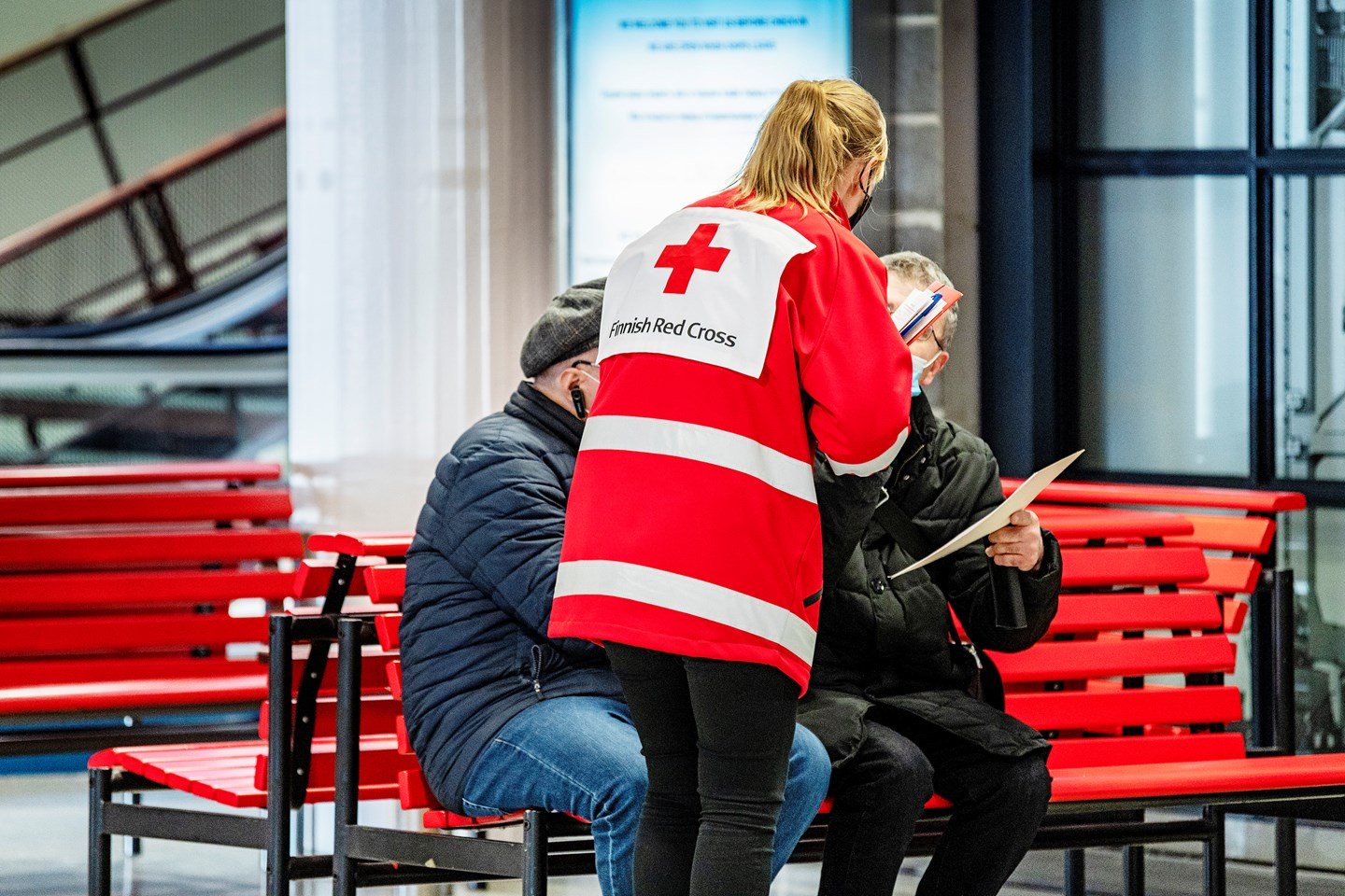 Volunteer wearing Red Cross clothing talking to refugees at the harbour.