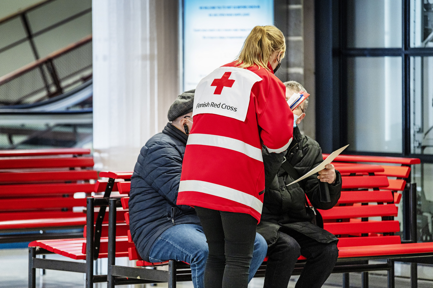 Volunteer wearing Red Cross clothing talking to refugees at the harbour.