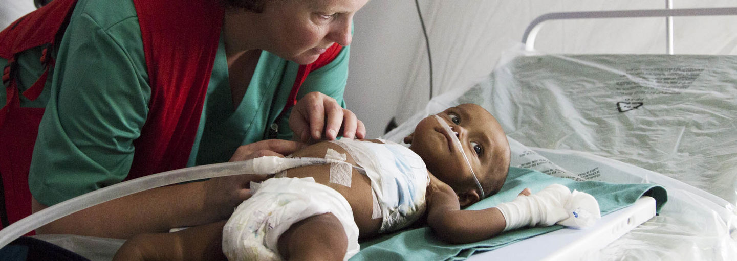 A Red Cross aid worker caring for a baby in a field hospital.