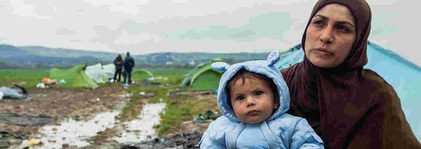 Mother holding a warmly-clad baby in her arms at a refugee camp.