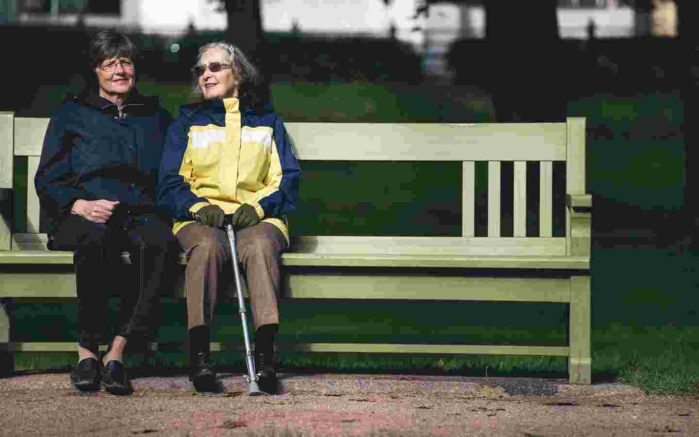 Two elderly women sitting side by side on a park bench.