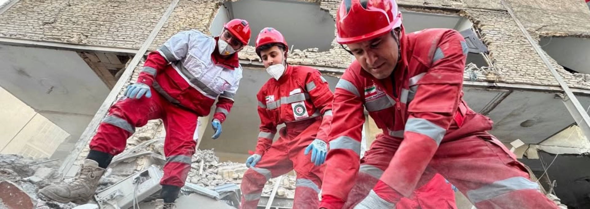 Two Red Cross volunteers in red vests, holding collection boxes. They are next to an about two-metre tall collection box.
