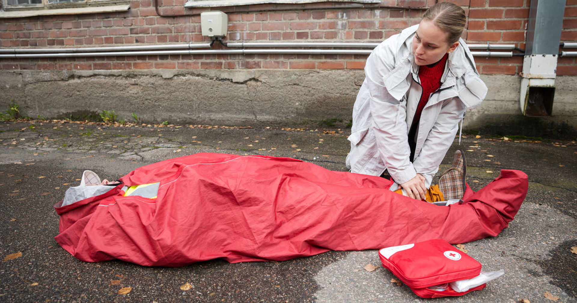 A person is lying in a thermal sleeping bag. Another person is providing first aid to them.