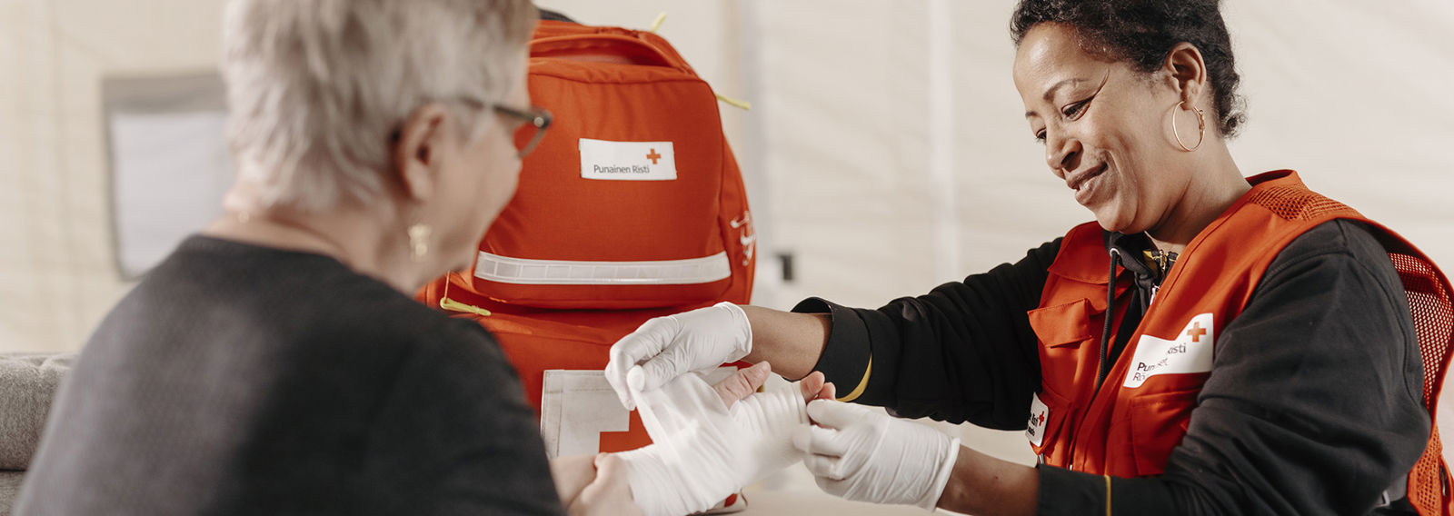 Two Red Cross ski slope volunteers wrapping a blanket around someone lying on the snow at the side of a ski slope.
