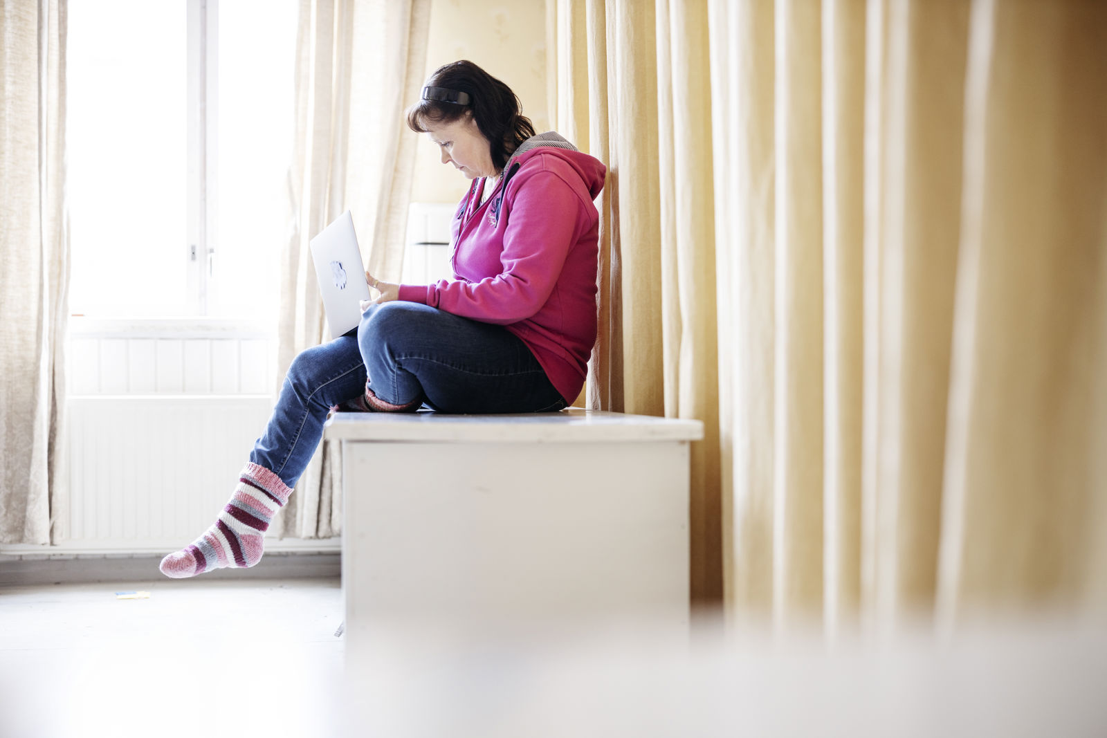 An online volunteer sits in front of a window with a laptop on their lap, typing.