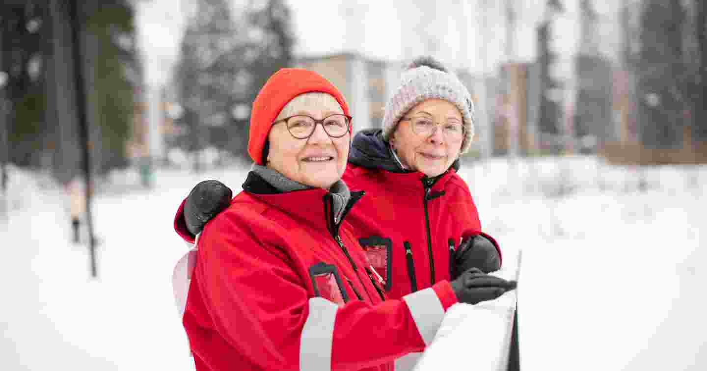 Red Cross volunteers Tuuli Sundell and Leena Valtee-Kuuskoski smiling side by side in a winter landscape.
