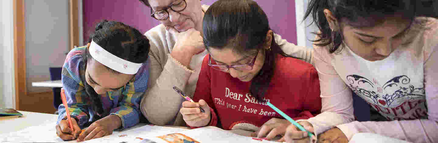 A woman is teaching three young immigrant girls.