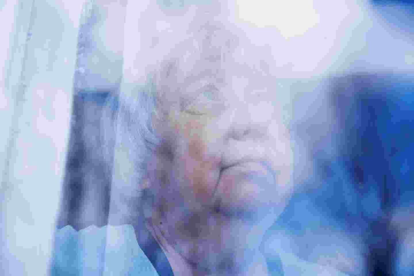 An elderly woman with a serious expression looking out of a window.