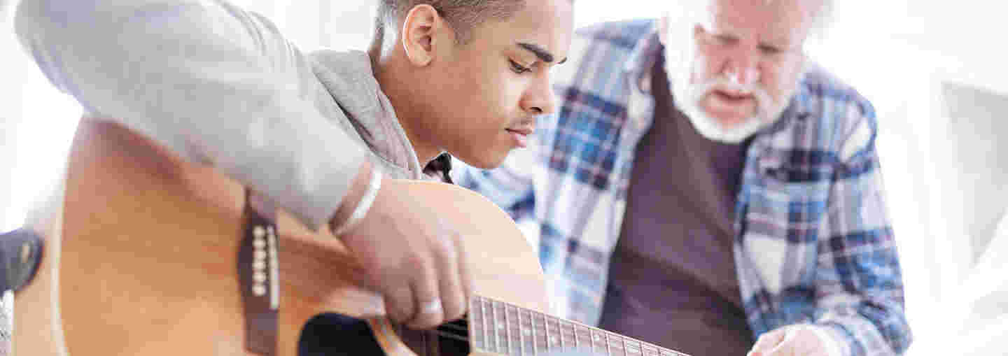 Young man learning to play the guitar with the assistance of an older man.